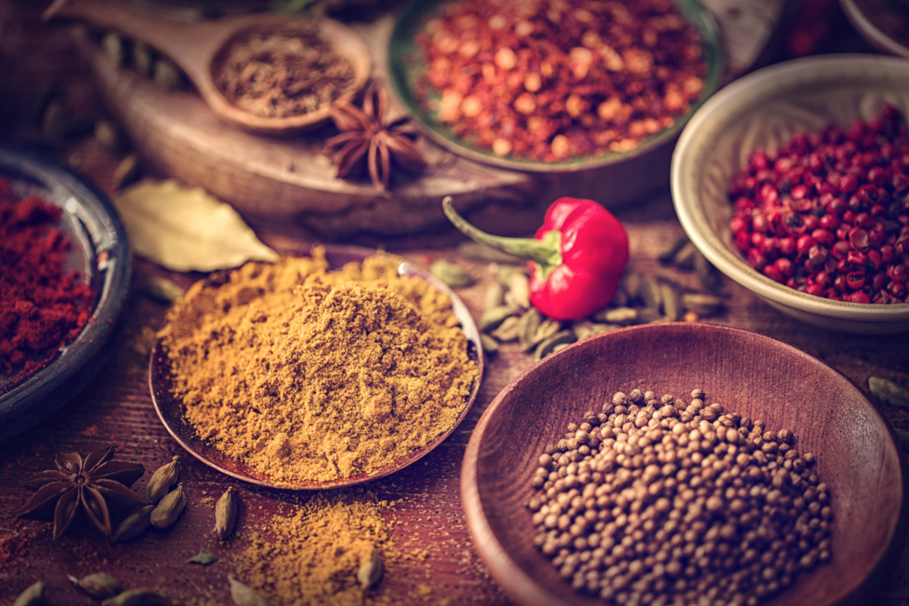 Variation of Spices and Herbs like chili peppers, parsley, rosemary, peppercorns, cayenne pepper, tumeric, cumin, garlic and ginger on wooden background