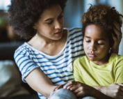 Young black mother taking care of her depressed little daughter at home.