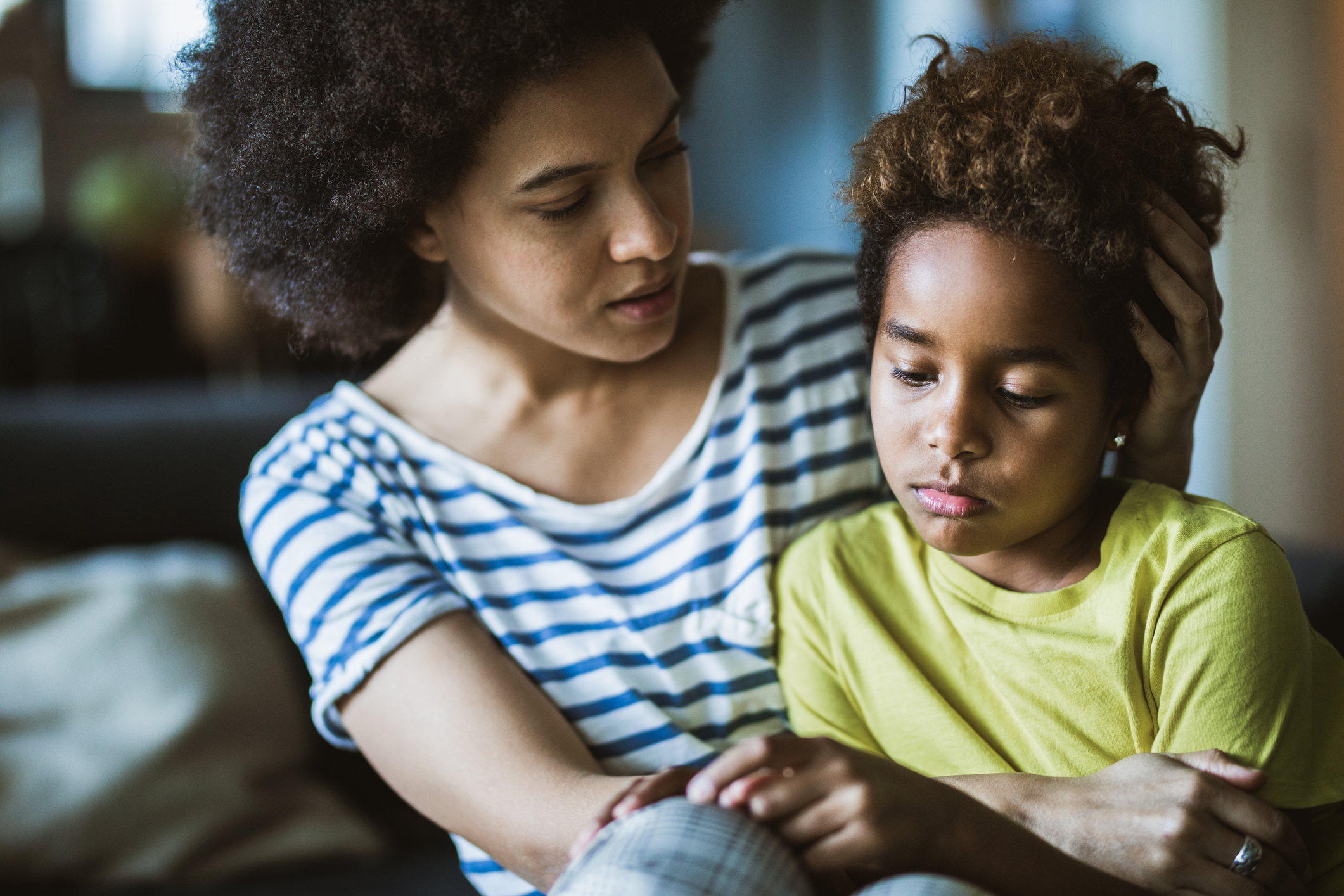 Young black mother taking care of her depressed little daughter at home.