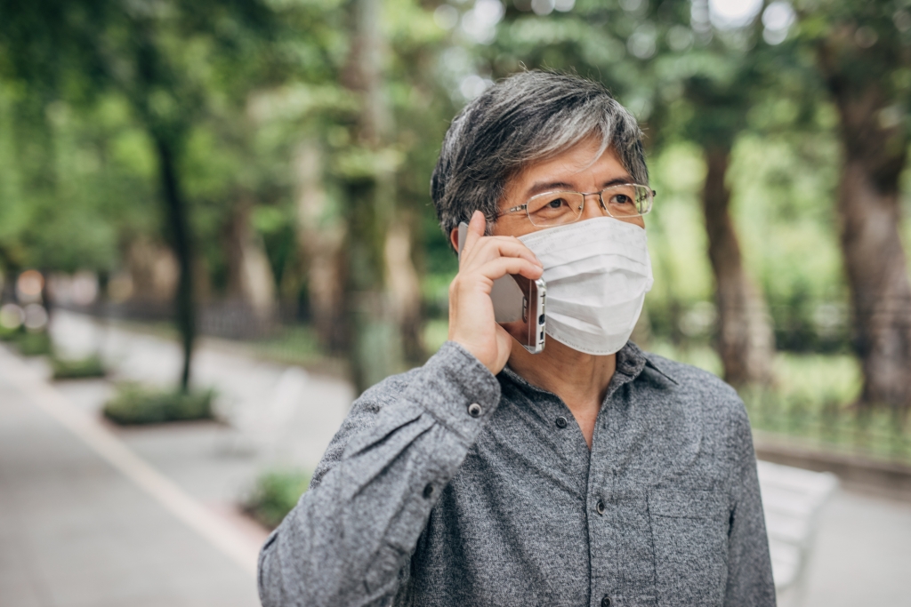 One man, mature man with surgical mask talking on mobile phone downtown in city.