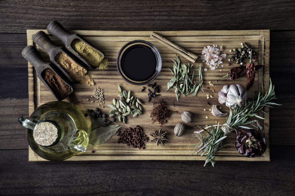 Variety of allspice ingredients and condiments for food seasoning on table in old fashioned kitchen. Ingredients set on a large size cutting board